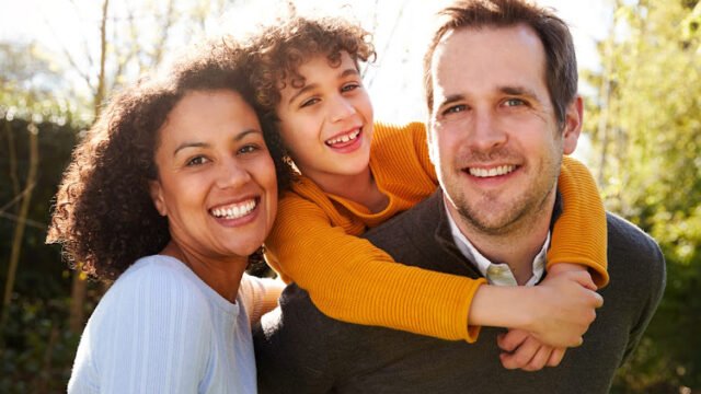 Outdoor Portrait Of Smiling Family In Garden At Home Against Flaring Sun