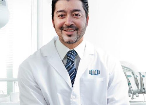 Portrait of happy male dentist wearing lab coat while sitting in clinic