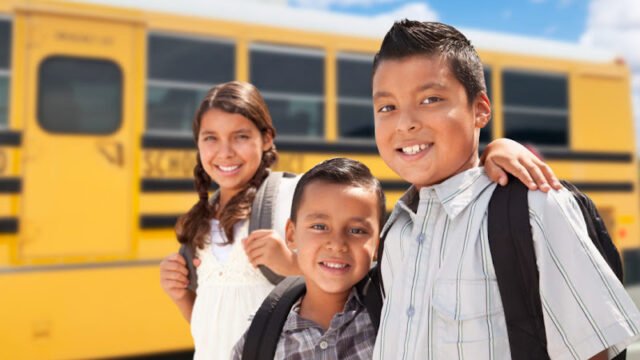 Young Hispanic Boys and Girl Walking Near School Bus.